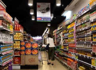 Jak skutecznie komunikować promocje wizualnie w punkcie sprzedaży Kobieta z wózkiem idzie alejką supermarketu pełną produktów i promocji.